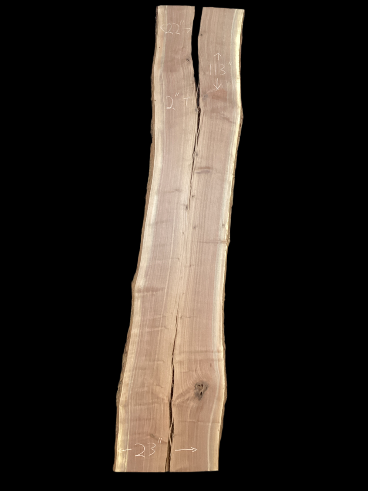 A long walnut wood slab with a split down the middle on a black background.