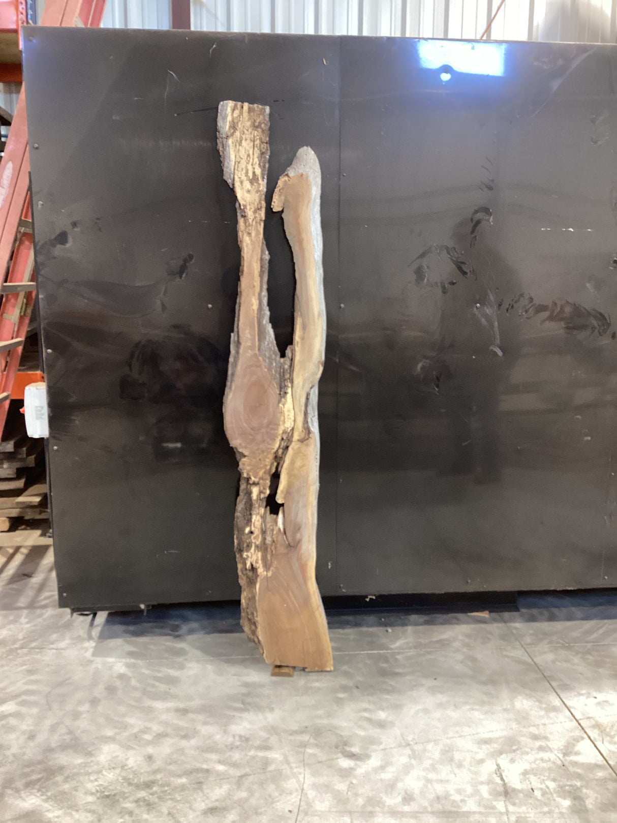 A walnut wood slab with a natural grain and unique river design leaning against a black metal bin.