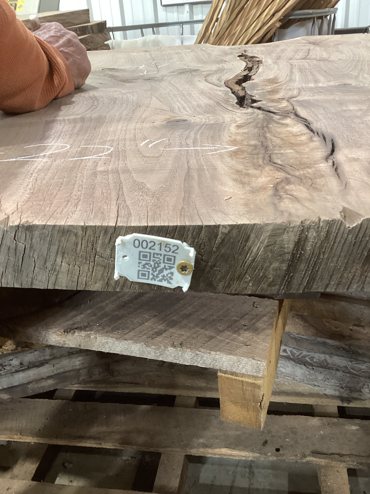 A walnut slab coffee table with visible grain patterns and natural edges, QR code attached, sitting on a pallet.