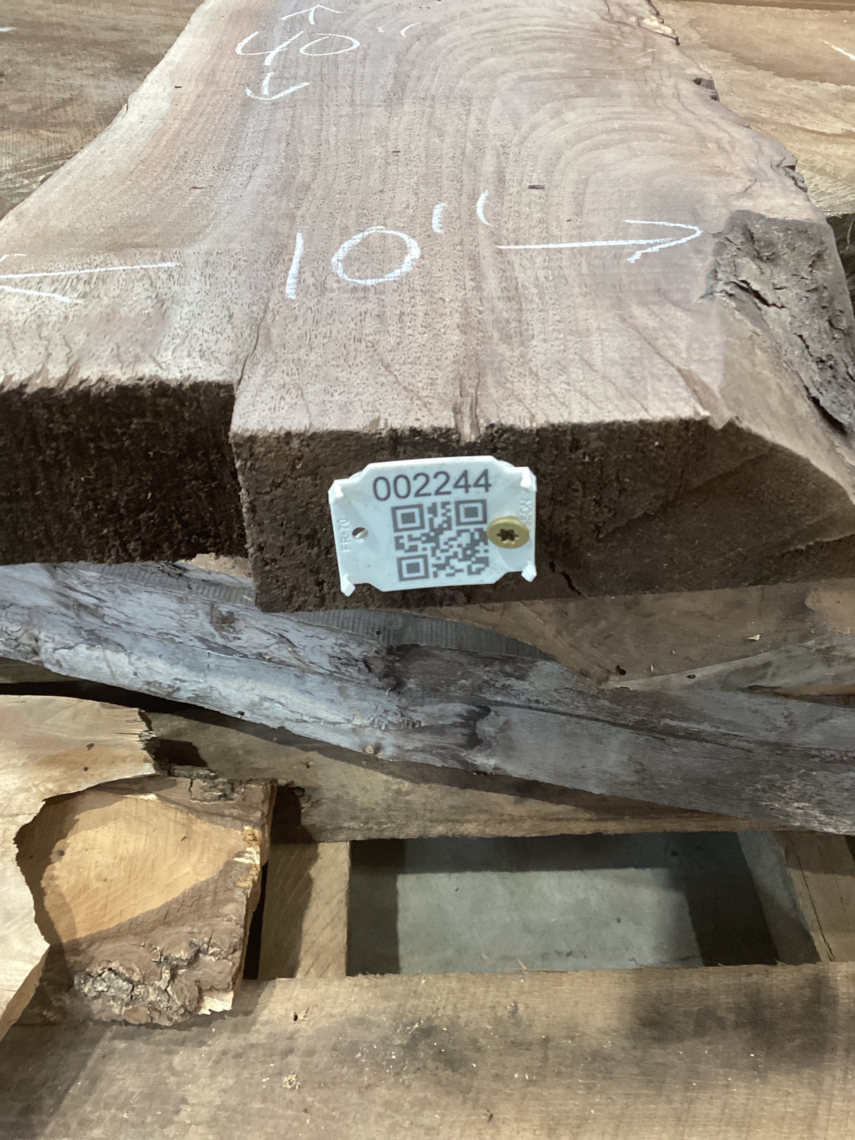 A walnut slab with a rugged edge and live edge, displaying natural wood patterns and a QR label with a number attached to it.