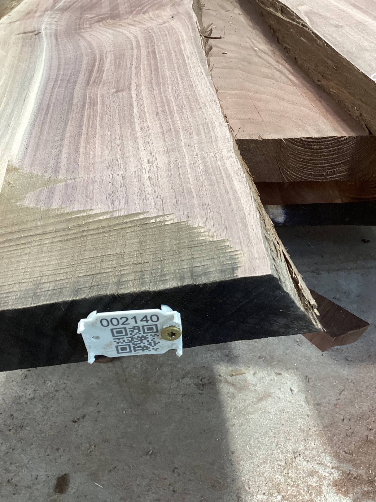 A walnut slab with a large split, featuring a QR tag with a barcode and measurements.