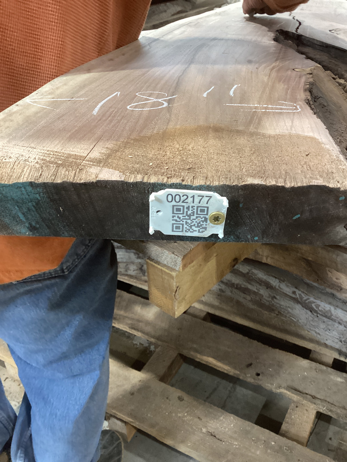 A walnut wood slab with a visible grain pattern, marked with a QR label, resting on a wooden pallet.