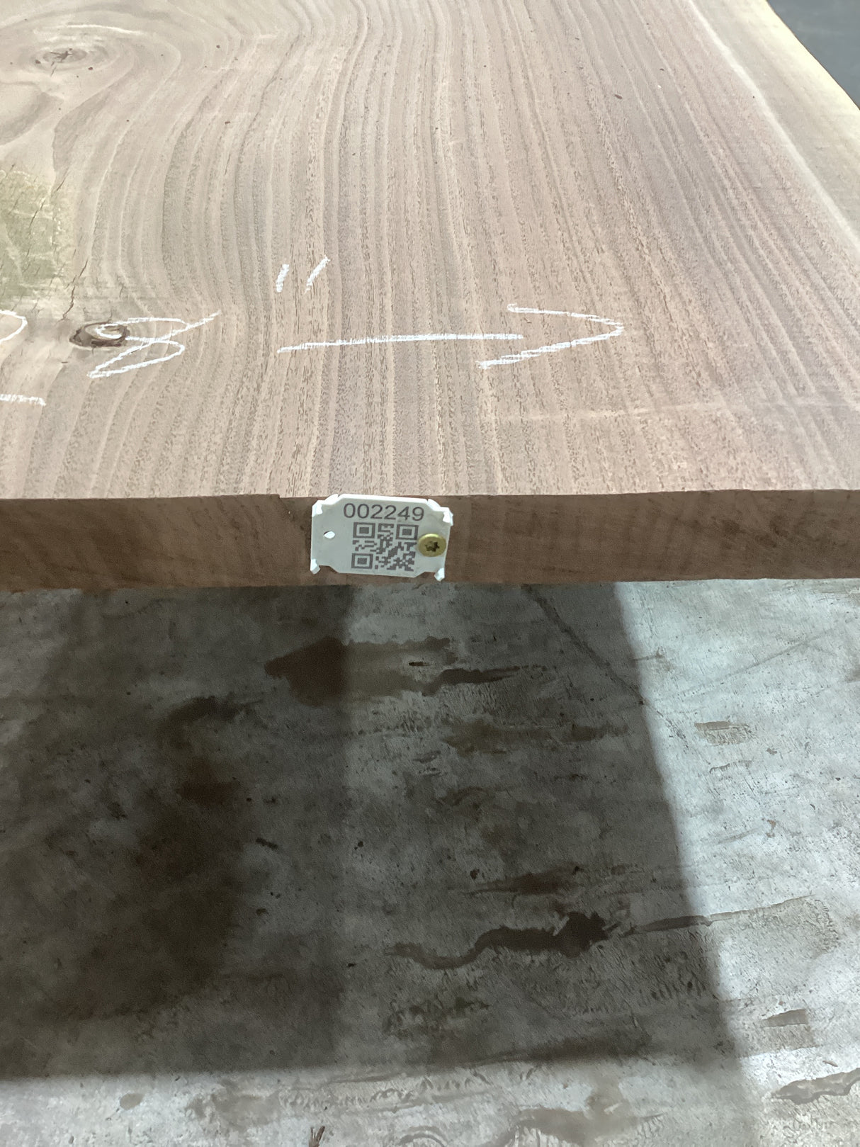 A walnut slab edge with visible wood grain, placed on a support structure, with a QR label attached.