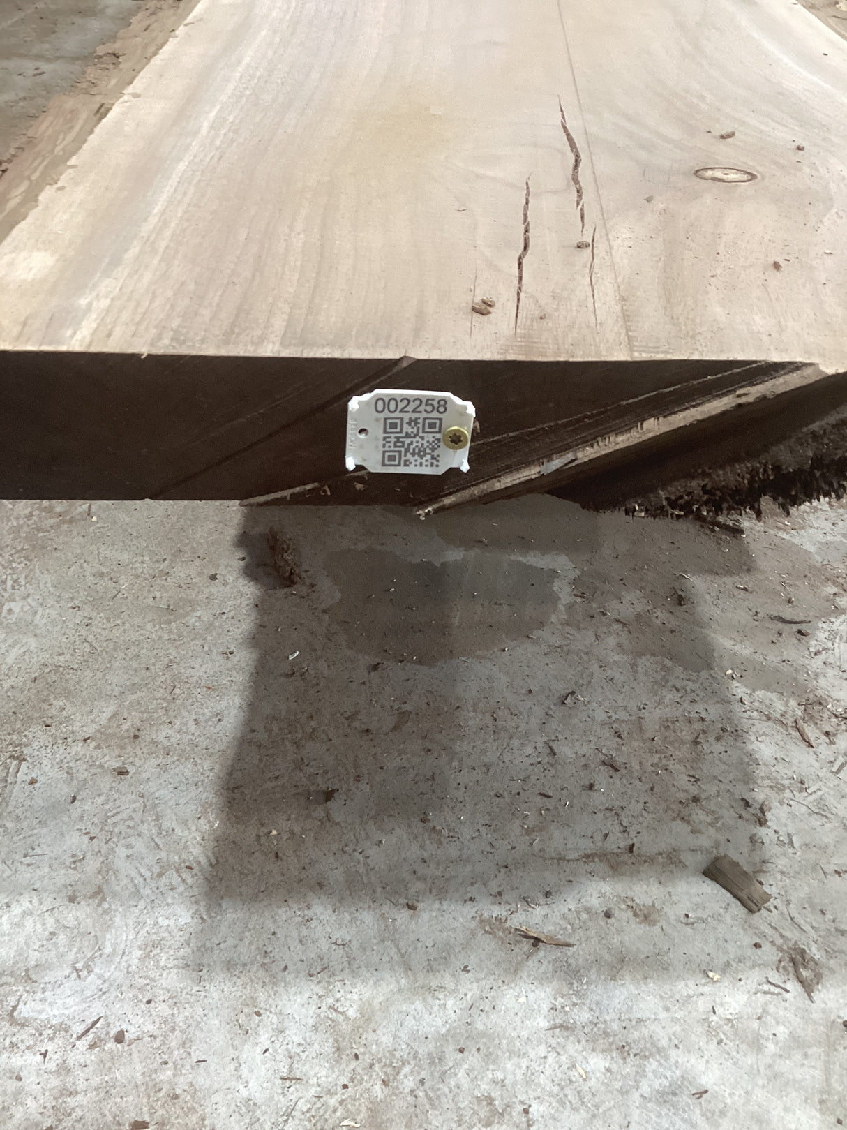 A solid walnut wood slab with visible grain and knots, placed on a concrete surface with a QR code of the sku.