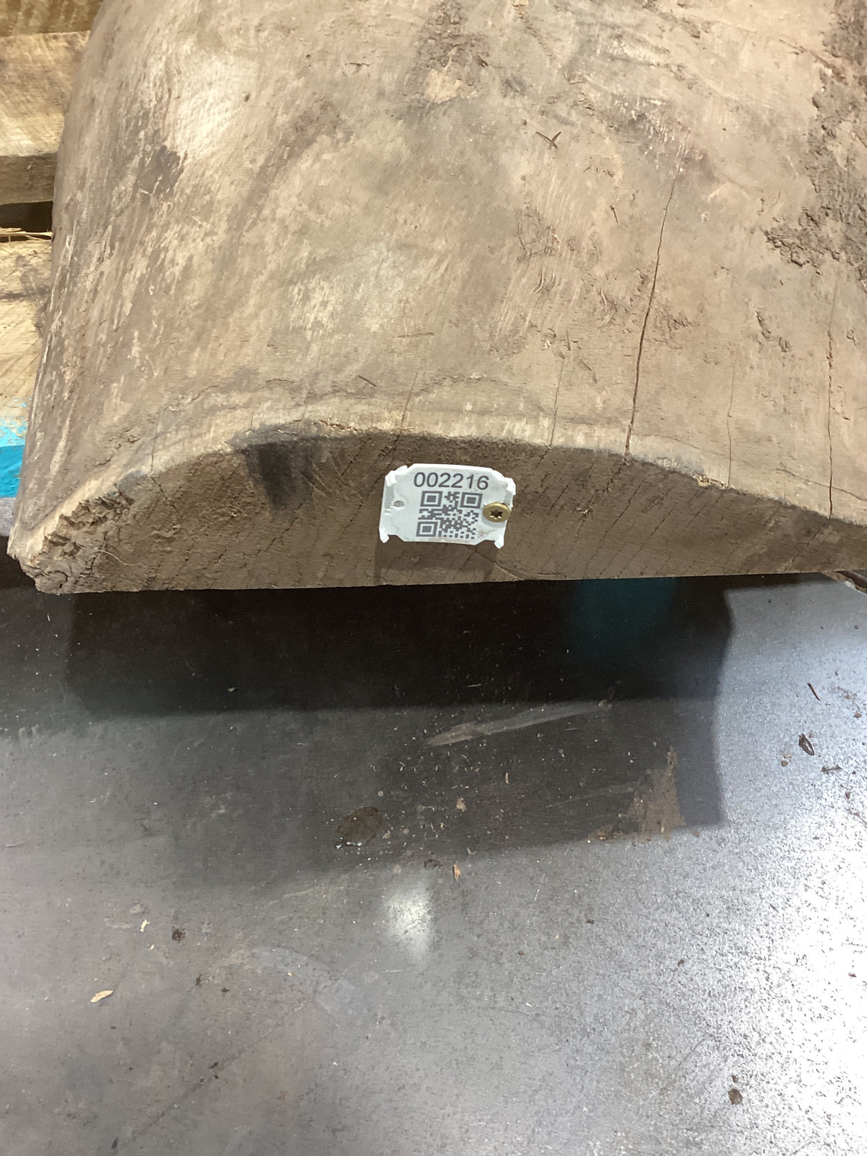 A rough, natural walnut slab edge with a QR label attached.