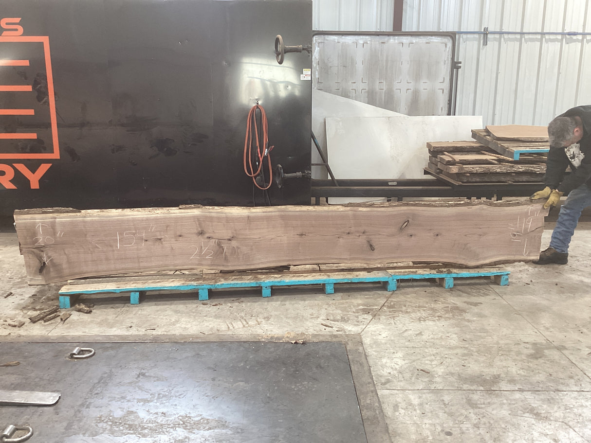 Large walnut wood slab propped on pallets with a man holding up one side.