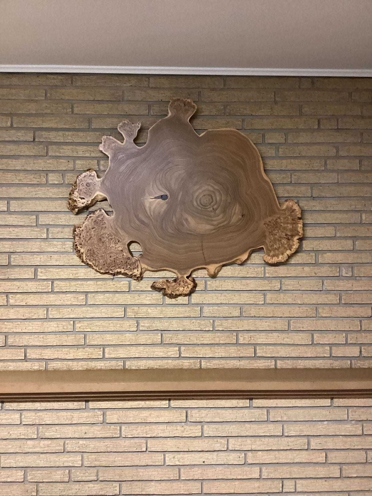 A circular wooden wall hanging art piece with a rustic finish mounted on a brick wall.
