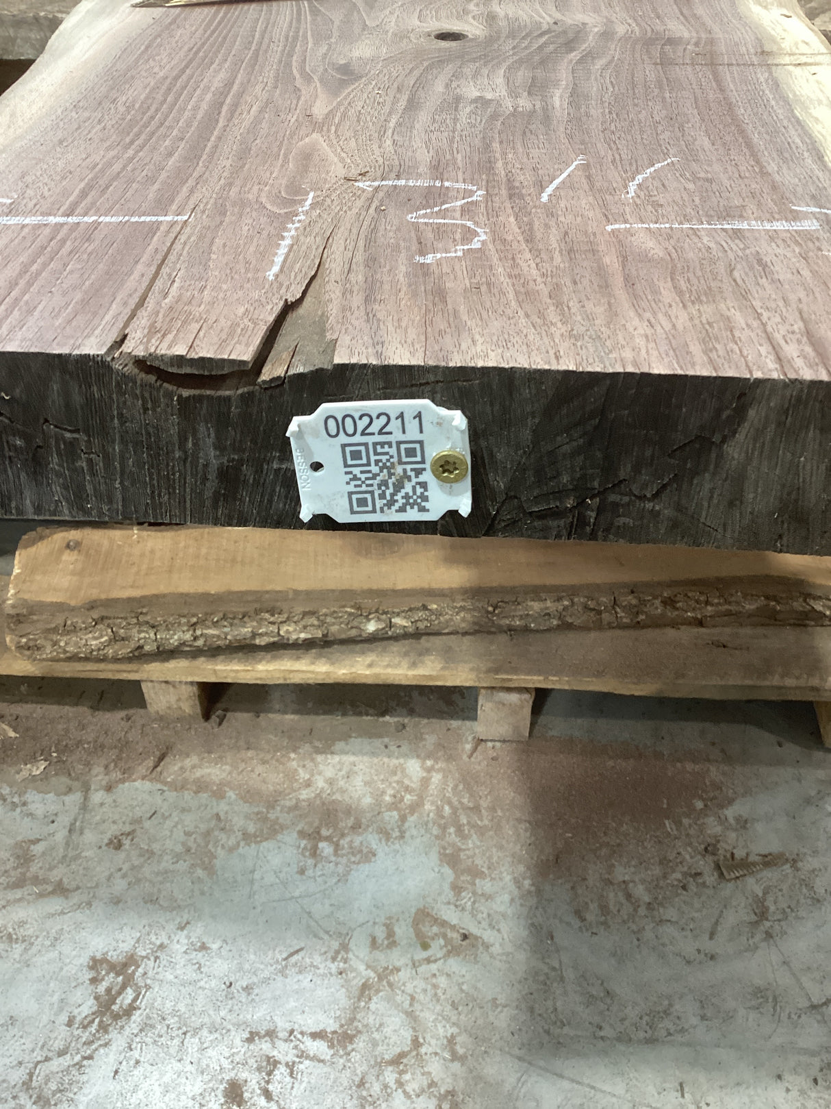 A walnut slab with a visible wood grain pattern and a QR tag attached to it, placed on a wooden pallet.
