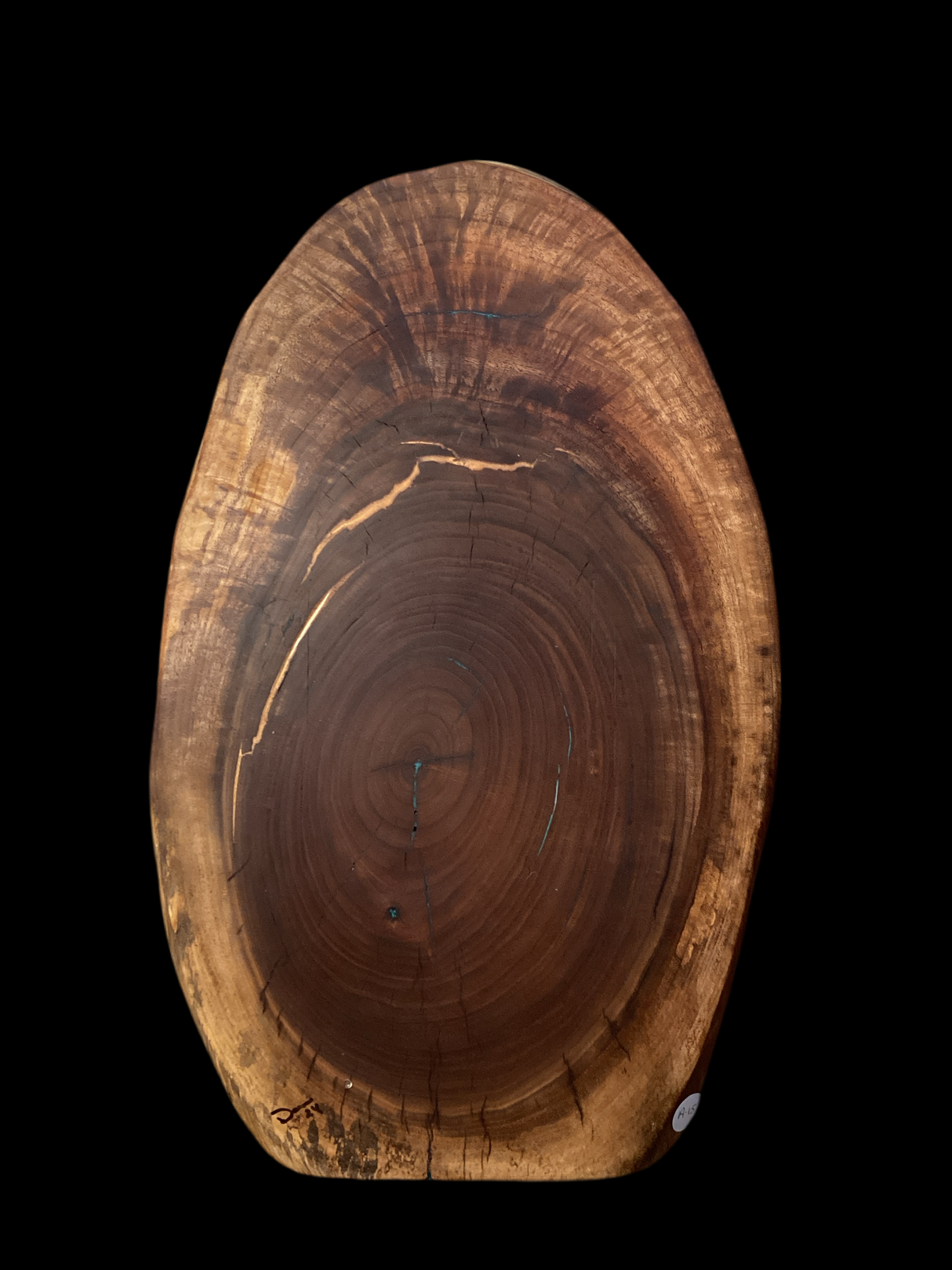 A round black walnut charcuterie board with turquoise and copper epoxy filled cracks on a white background.