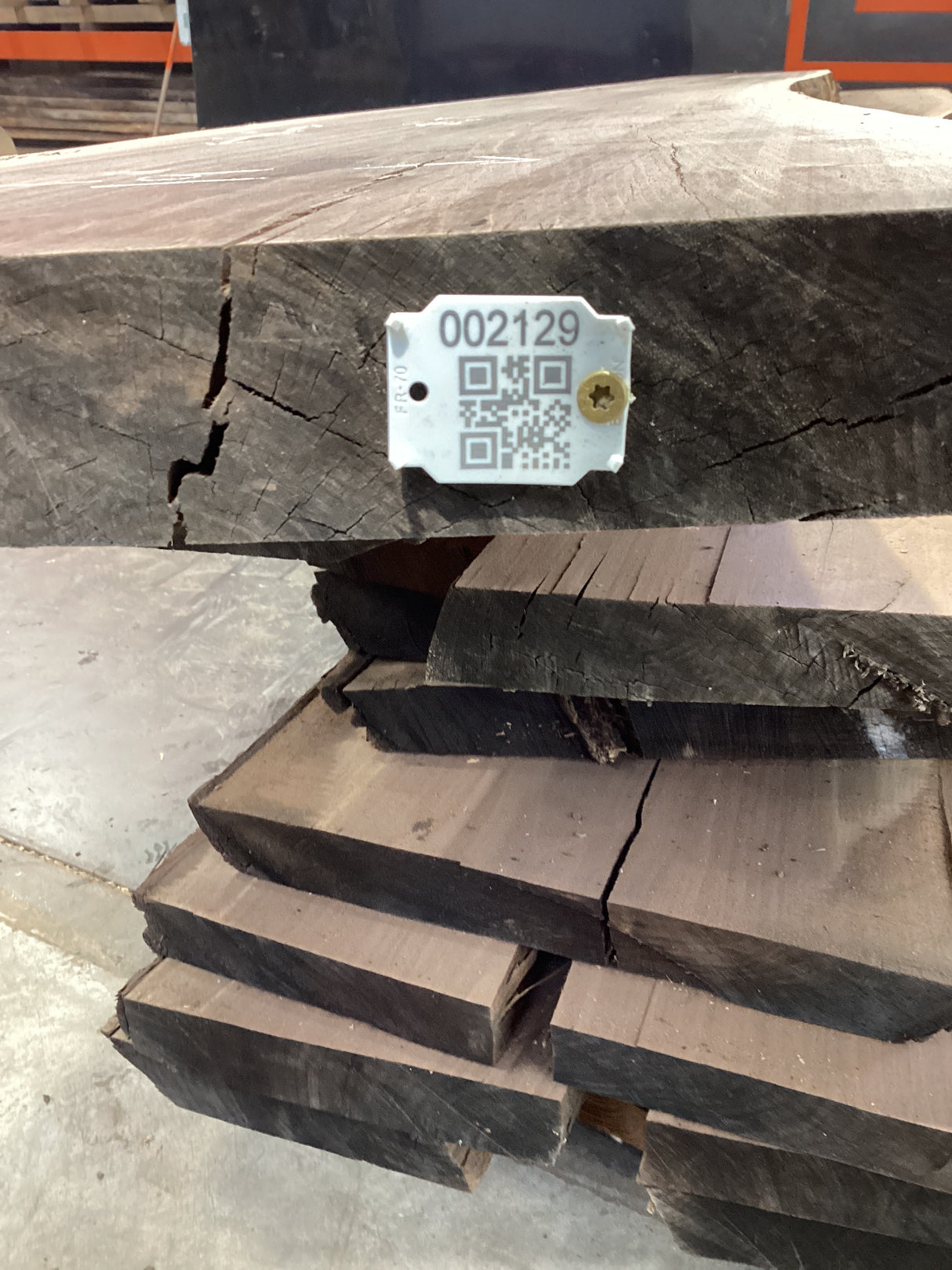 A walnut wood slab with a visible QR code on a tag attached to it, placed among other slabs.