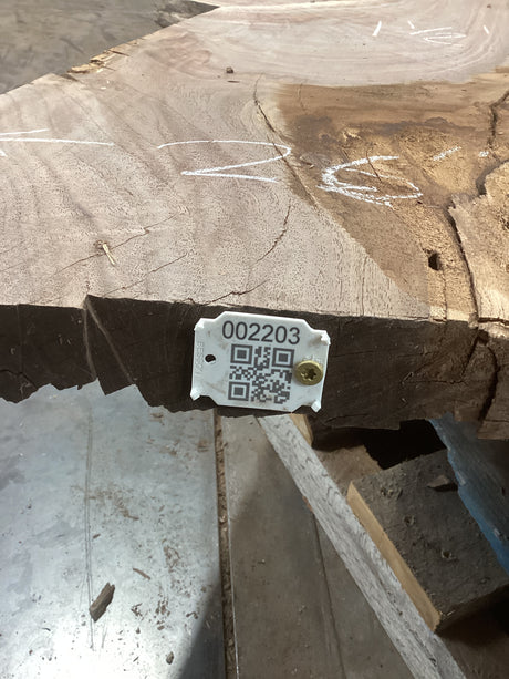 A walnut wood slab with a visible wood grain and a tag with a QR code attached to it.