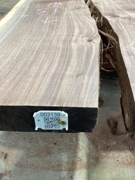 A walnut wood slab with visible splits on the ends, marked with a tag containing identification information.
