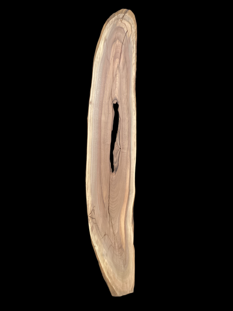 A long walnut slab with a long hole down the middle and on a black background. 