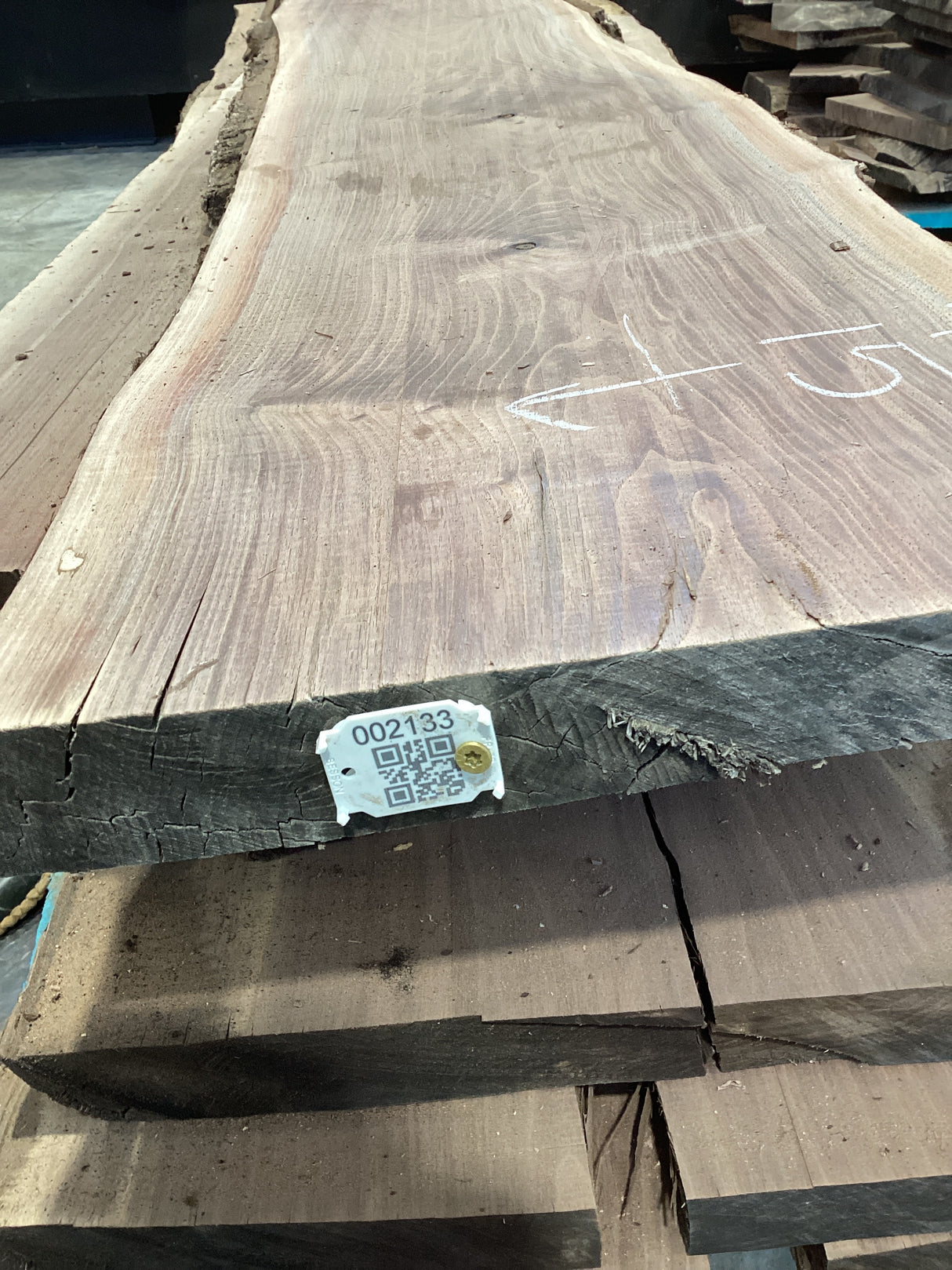 A walnut slab with a natural edge, laid flat on a surface, with a tag attached to one end displaying a barcode and product information.