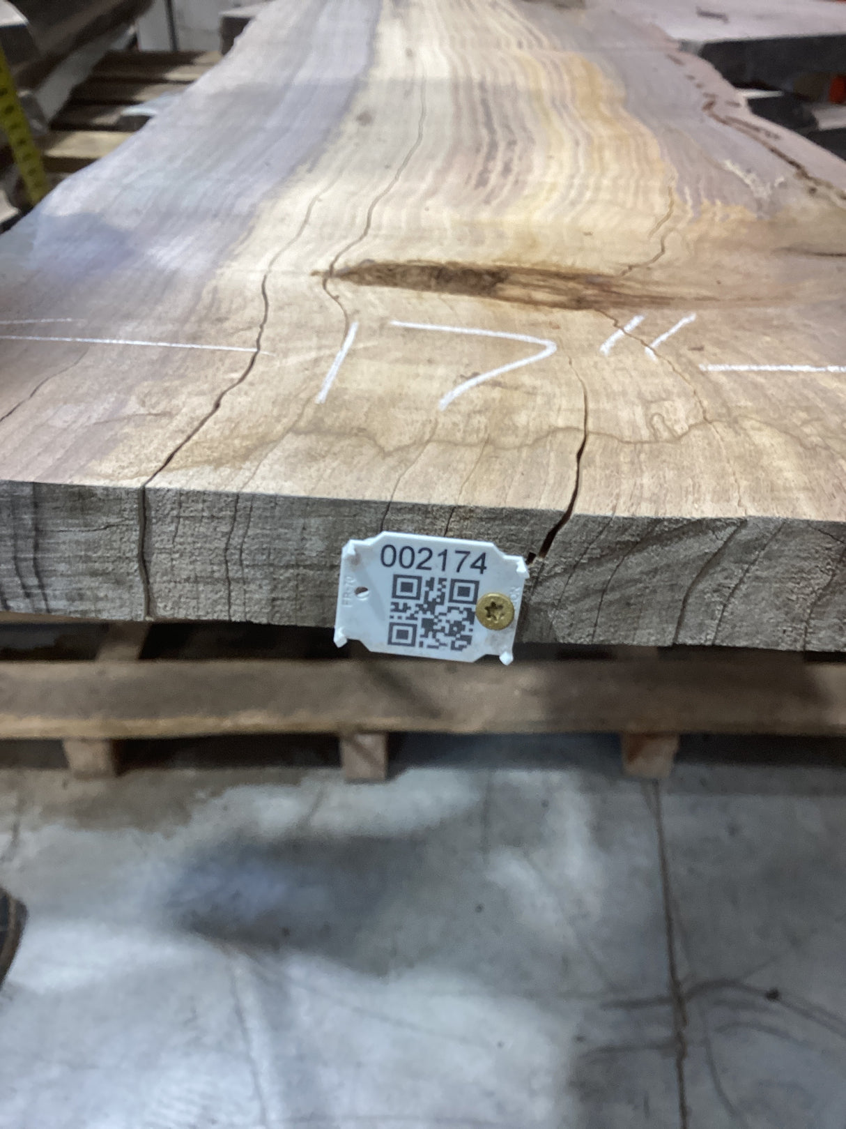A walnut slab with visible cracks and a QR tag attached to it, placed on a wooden surface.