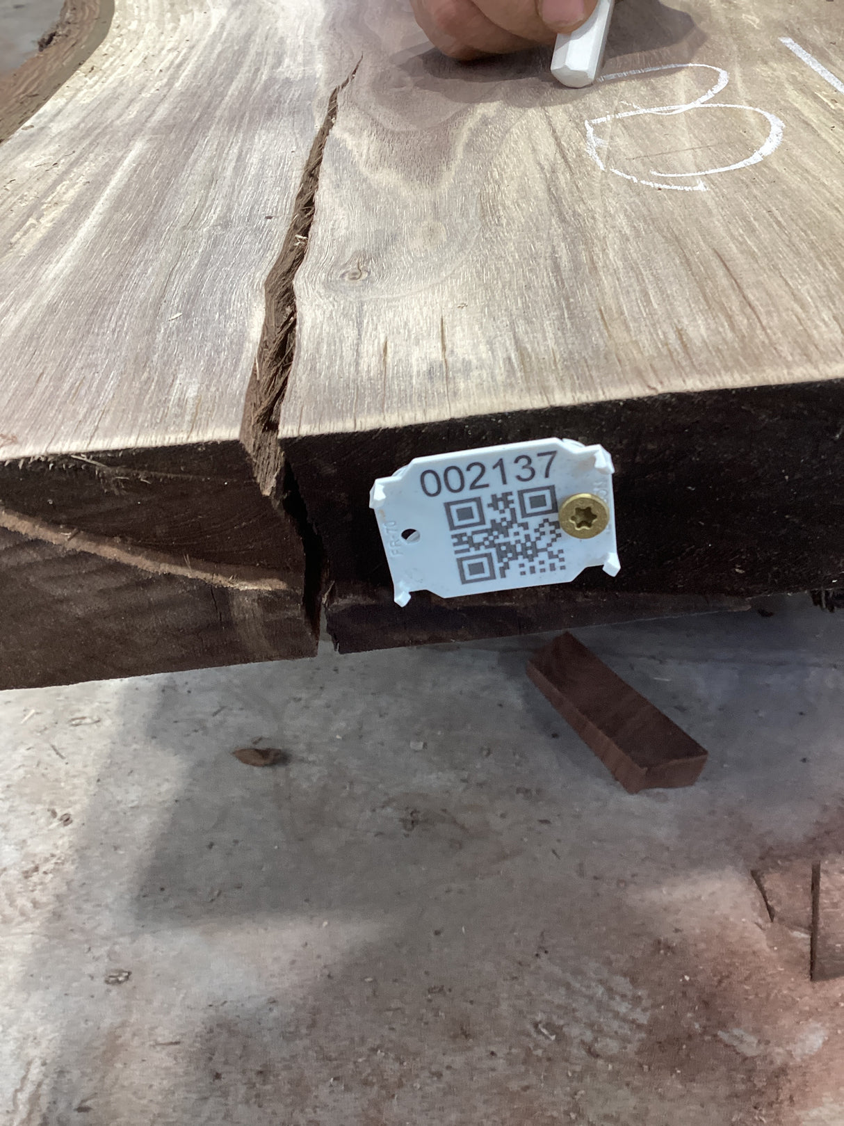 A walnut slab with a large crack running through it, featuring a white label with a QR code attached to the side.