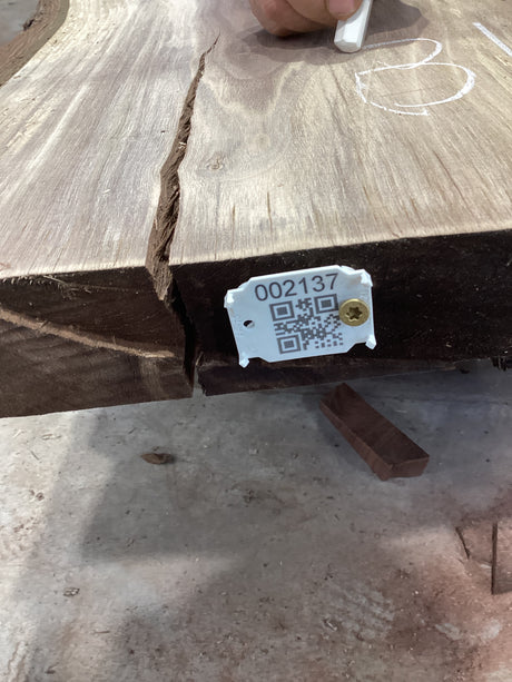 A walnut slab with a large crack running through it, featuring a white label with a QR code attached to the side.
