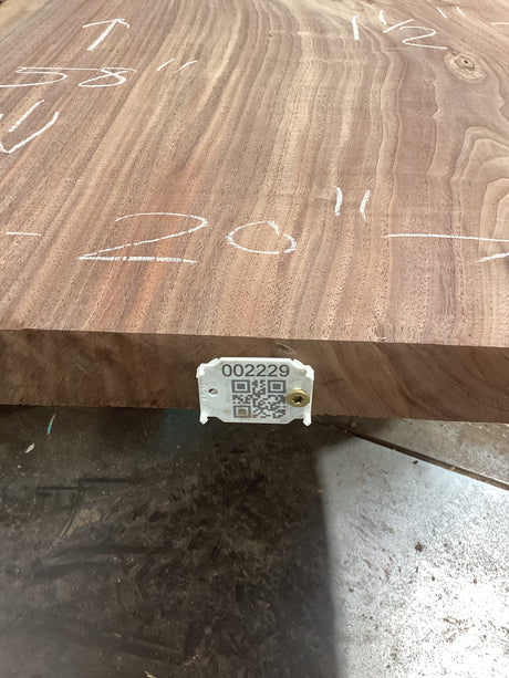 A walnut wood slab with visible growth rings and a QR label attached to it.