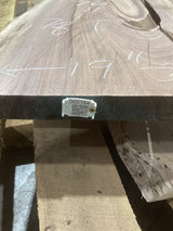A walnut wood slab with visible natural patterns and a QR label on the edge. The slab is placed on a wooden support structure, and there are measurements marked on the surface.