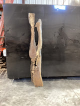 A walnut wood slab with a natural grain and unique river design leaning against a black metal bin.