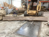 A walnut wood slab propped on a forklift showing its length.