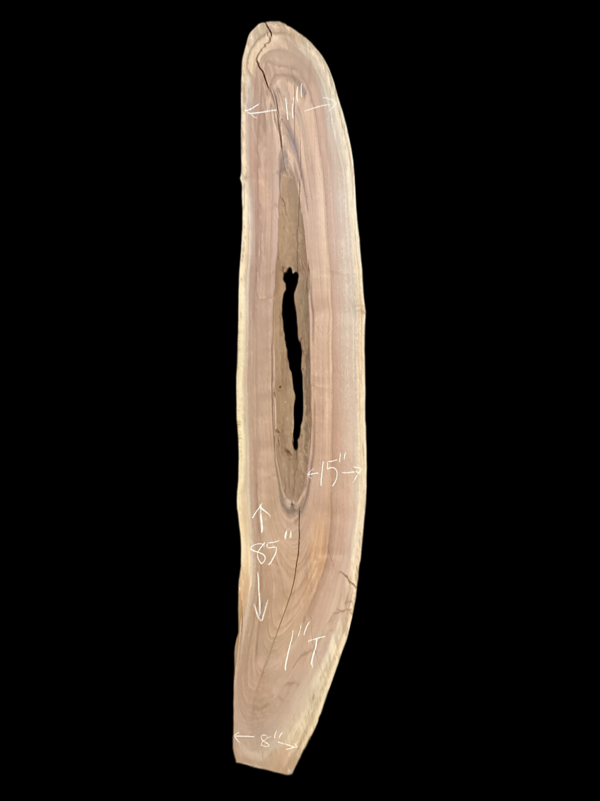 A long walnut slab with a long hole down the middle and on a black background. 