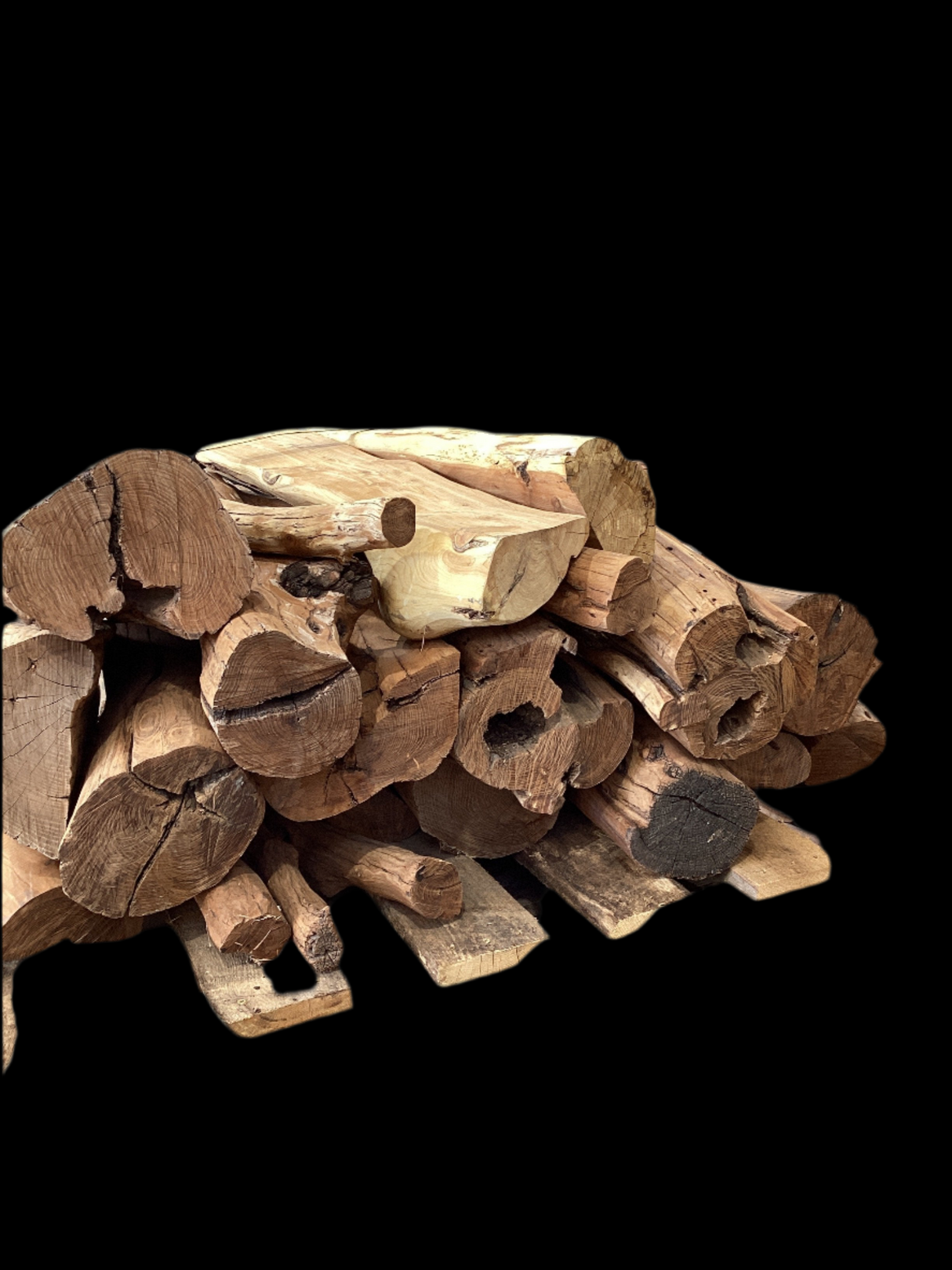 A pile of rough-sanded, debarked Osage Orange wood table legs stacked on a wooden pallet in a warehouse setting.