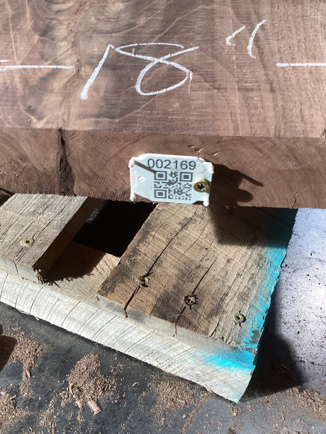 A walnut slab with visible natural figures, placed on a wooden support with a visible QR code on the surface.