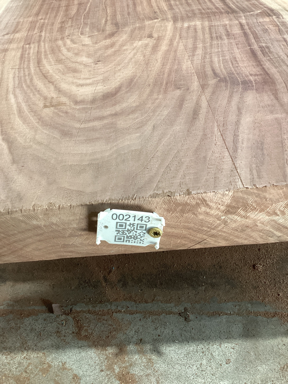 A walnut slab with a visible live edge and a QR tag attached to it indicating a product identification number.