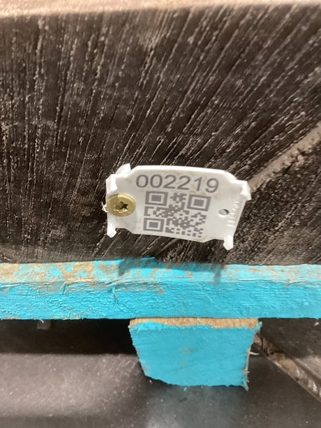 A close-up of a walnut slab showing a tag with a QR code and a serial number attached to it, indicating its authenticity and quality.