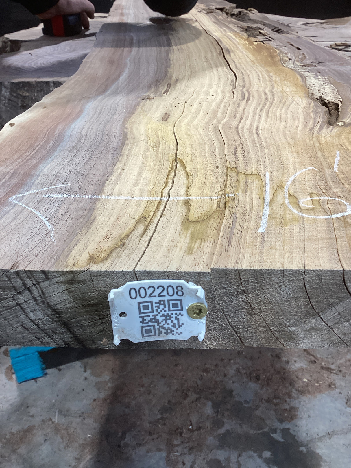 A walnut slab with visible natural color contrast and growth rings, marked with a tag containing a QR code.