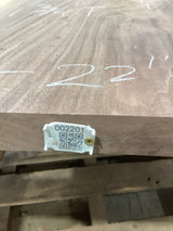 A walnut wood slab with a visible label that has a QR code and the number 002201 written on it. The slab is placed on a stack of wood in a workshop setting.