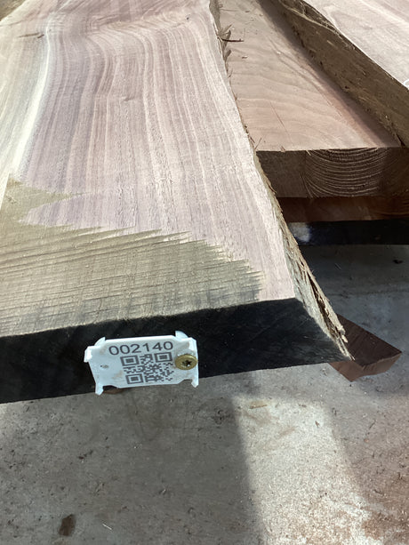 A walnut slab with a large split, featuring a QR tag with a barcode and measurements.