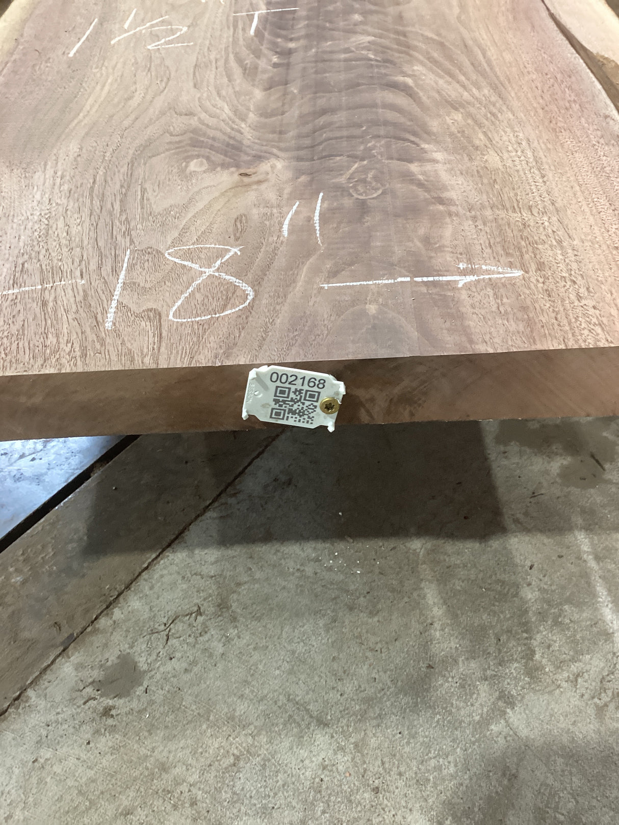 A walnut wood slab with visible knots and natural edge, with a QR label attached.