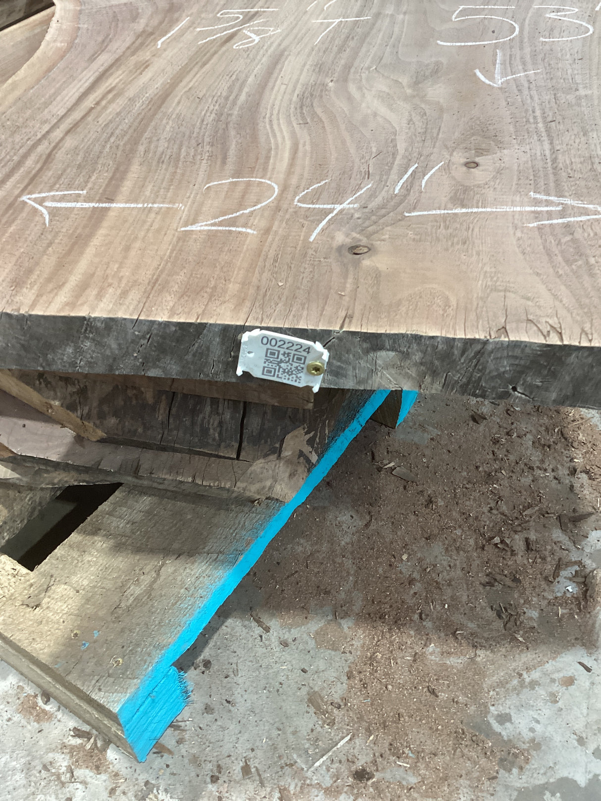 A walnut wood slab with visible grain patterns, marked with measurements on the surface, and a QR label attached.