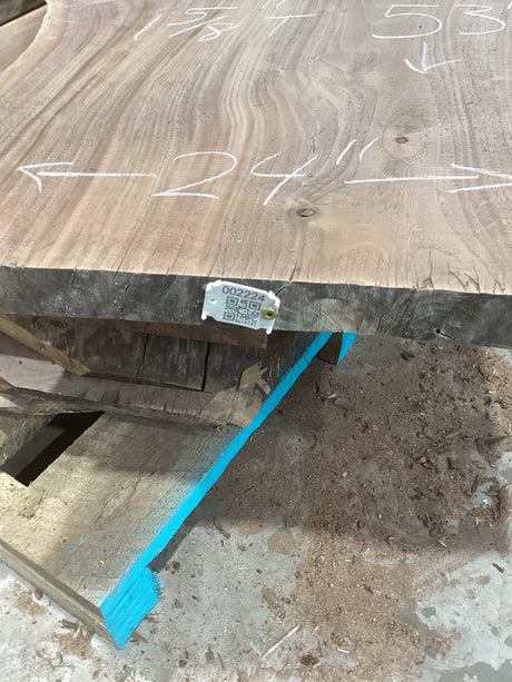 A walnut wood slab with visible grain patterns, marked with measurements on the surface, and a QR label attached.