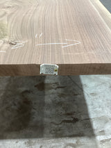 A walnut slab edge with visible wood grain, placed on a support structure, with a QR label attached.