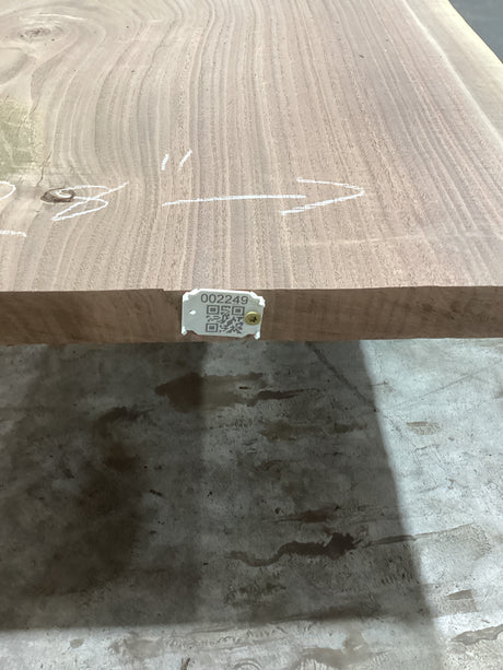 A walnut slab edge with visible wood grain, placed on a support structure, with a QR label attached.