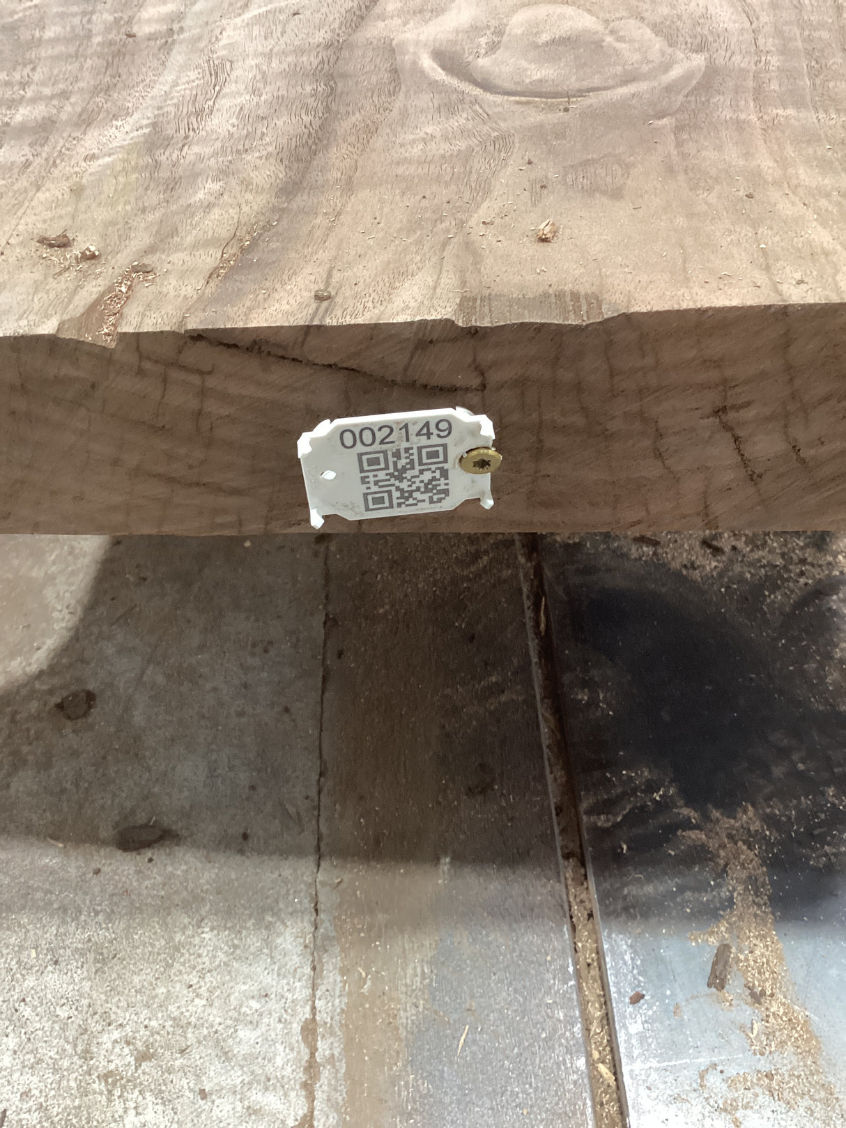 A walnut slab with a visible QR label attached to it, placed on a metal support structure, likely in a workshop or construction setting.