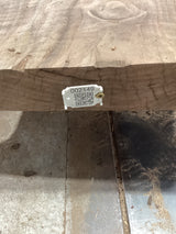 A walnut slab with a visible QR label attached to it, placed on a metal support structure, likely in a workshop or construction setting.