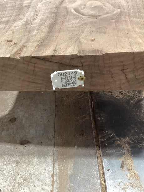 A walnut slab with a visible QR label attached to it, placed on a metal support structure, likely in a workshop or construction setting.