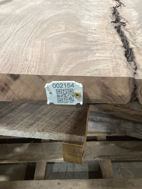 A walnut slab with a visible wood grain and a bark inclusion, marked with a tag containing a QR code.