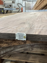 A walnut wood slab with a visible wood grain and a QR tag attached to it, placed on a wooden surface.