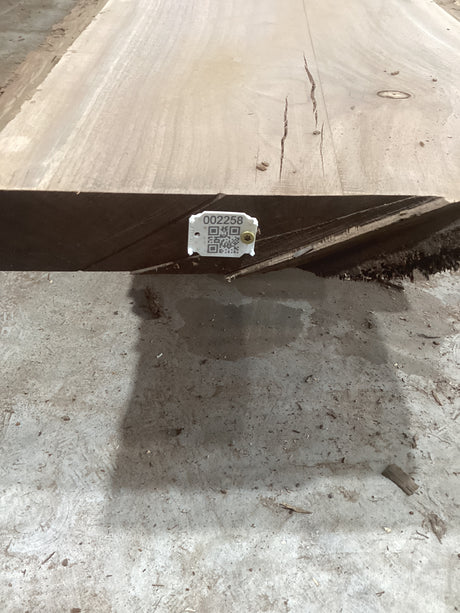 A solid walnut wood slab with visible grain and knots, placed on a concrete surface with a QR code of the sku.