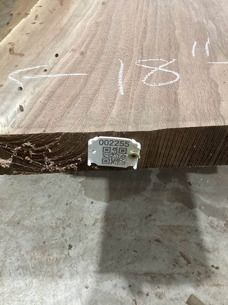 A walnut wood slab with a visible growth ring pattern, marked with white chalk measurements, a QR code, and a label.