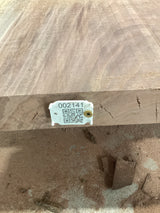 A walnut slab with a visible live edge and a tag with a QR code attached to it.