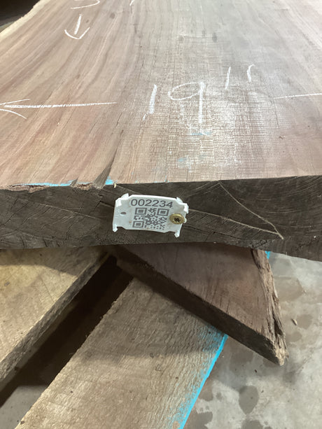 A walnut wood slab with a visible QR label attached to it, placed on a metal rack.
