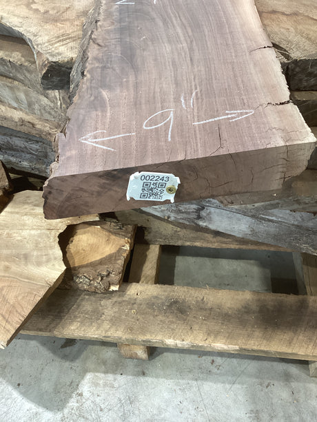A rough-cut walnut wood slab with visible grain patterns, marked with a QR label attached to the edge.