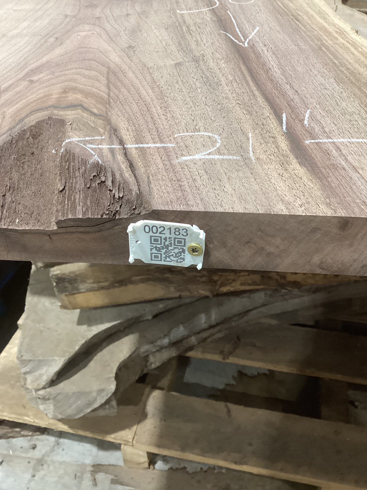 A walnut wood slab with a QR tag attached to it, placed among other slabs, with markings on the wood surface.