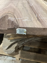 A walnut wood slab with a QR tag attached to it, placed among other slabs, with markings on the wood surface.